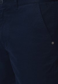 Granatowe chinosy wykonane z tkaniny wplecionej, z przednią kieszenią z małym metalowym logo i gładką fakturą.