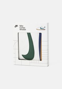 Nike Cortez håndledsrem i et hvidt quiltet design, med et stort grønt swoosh, blå og guld accenter, præsenteret i en grafisk pakke.
