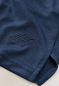 Pantaloni corti blu navy realizzati in un tessuto testurizzato con un sottile motivo a righe. Presentano un logo ricamato vicino all'orlo e fessure laterali.