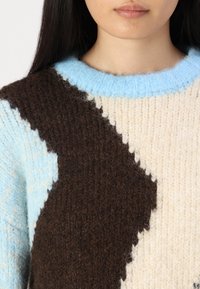 Sweter dziany z wzorem w zygzaki w odcieniach brązu, jasnoniebieskim i kremowym, z okrągłym dekoltem i miękkim, teksturowanym wełnianym materiałem.