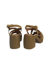 Brown suede platform sandals with crisscross straps and a chunky heel. The buckle is metallic, and the sole features a smooth finish.