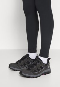 Scarpe da trekking nere con pannelli in rete e dettagli rosa, dotate di suole e lacci texturizzati, abbinate a leggings neri e calze bianche.