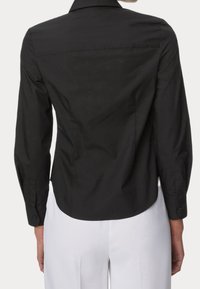 Camisa negra de cuello con mangas largas, diseño ajustado, textura suave y puños abotonados. Corte más corto en la parte trasera con un dobladillo redondeado.