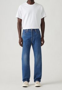 Vit kortärmad T-shirt kombinerad med blå denimjeans. Jeansen har rak skärning, femficksdesign och subtila bleknade detaljer.