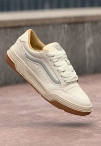 Lys beige sneaker med en glatt skinnoverdel, grå detaljer, perforert tådesign og en teksturert gummisåle. Inkluderer snøringer og polstret krage.