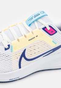 Chaussure de course Nike Pegasus 40 blanche avec swoosh bleu, accents jaune clair, languette bleue et lacets blancs sur fond blanc.