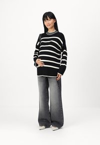 Svart-hvitt stripete oversized strikkegenser med lange ermer, kombinert med høyt liv grå flared jeans og spisse hvite sko.
