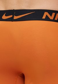 Leggings atléticos laranja com uma cintura preta e um logo da Nike laranja. Textura suave sem padrões ou acentos visíveis.