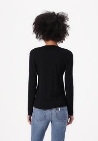 Maglietta nera a maniche lunghe con scollatura rotonda, design aderente e texture morbida. Abbinata a jeans azzurri chiari con tasche posteriori.