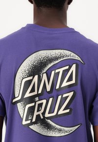 Purple cotton t-shirt featuring the text "SANTA CRUZ" in bold black and white font, set against a crescent moon graphic.