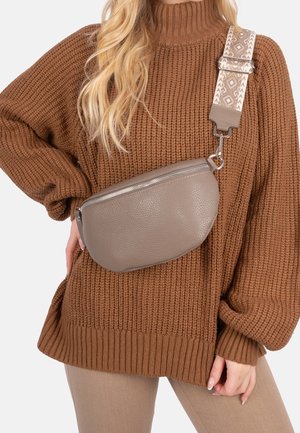 Femme portant un pull en grosse maille marron et un pantalon beige avec un sac bandoulière en cuir taupe avec une sangle ajustable à motif.