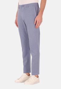 Lichtblauwe smalle broek met zijzakken, riemlussen en subtiele steken. G gedragen met witte sneakers.