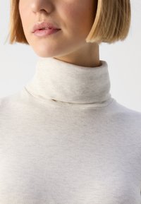 Cream turtleneck sweater with a soft ribbed texture. The fabric is thin and fitted, highlighting a high collar and simple, clean design.