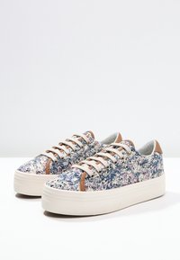 Sneakers med ett flerfärgat, spräckligt tygövre, beige gummisulor och bruna läderaccenter på hälen och snörningsområdet.