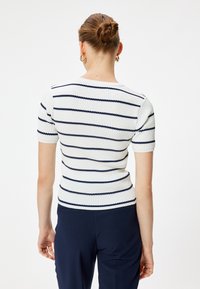 Hvid og marineblå stribet strik t-shirt med korte ærmer, der har et tekstureret stof og en tætsiddende pasform. Bagview viser en rundet krave.