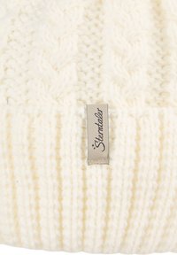 Off-white knitted woolen fabric with ribbed and cable knit patterns and a small beige tag reading "Sterntaler."