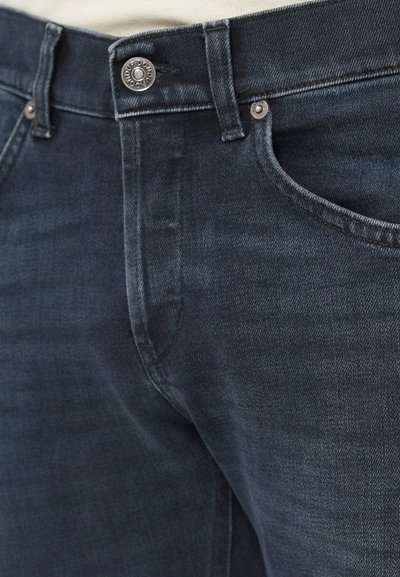 Κοντινή λήψη σκούρων μπλε τζιν παντελονιών που δείχνει την μπροστινή τσέπη, τους βρόχους της ζώνης, τις ραφές και τις λεπτομέρειες από μεταλλικά κουμπιά και καρφιά.