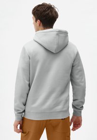 Lys grå hættetrøje med en rummelig hætte, ribbede manchetter og kant. Behageligt fleece-materiale, sømløst bagdesign, båret med lysebrune cargo-bukser.