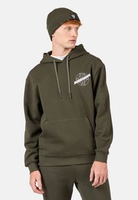Felpa verde oliva realizzata in misto cotone con tasca frontale, cappuccio con cordino e grafica del logo bianco. Abbinata a pantaloni coordinati.