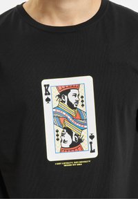 Black T-shirt featuring a colorful King of Spades graphic. The design includes detailed illustrations and text “I GOT LOYALTY, GOT ROYALTY INSIDE MY DNA.”