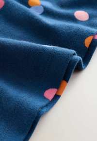 Gros plan sur un tissu bleu avec des pois colorés et une couture visible sur un bord plié.
