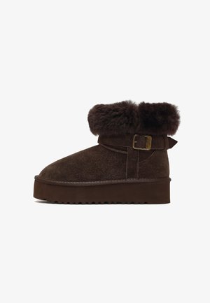 Brown suede boot with a fur cuff, a side buckle detail, and a thick, textured sole. Features a rounded toe and short ankle height.