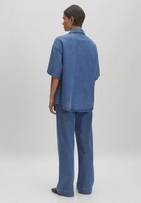 Denim oversized shirt en wijde broekset in lichtblauw. Zachte textuur, korte mouwen en een ontspannen pasvorm met zichtbare stikdetails.