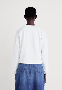 Sudadera blanca con cuello redondo, hombros caídos y puños acanalados. Combinada con una falda larga de denim azul que posee bolsillos traseros.