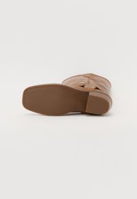 Botte en cuir marron avec une finition lisse, bout arrondi, petit talon et une sangle décorative sur le côté. Semelle en caoutchouc plate pour une bonne adhérence.
