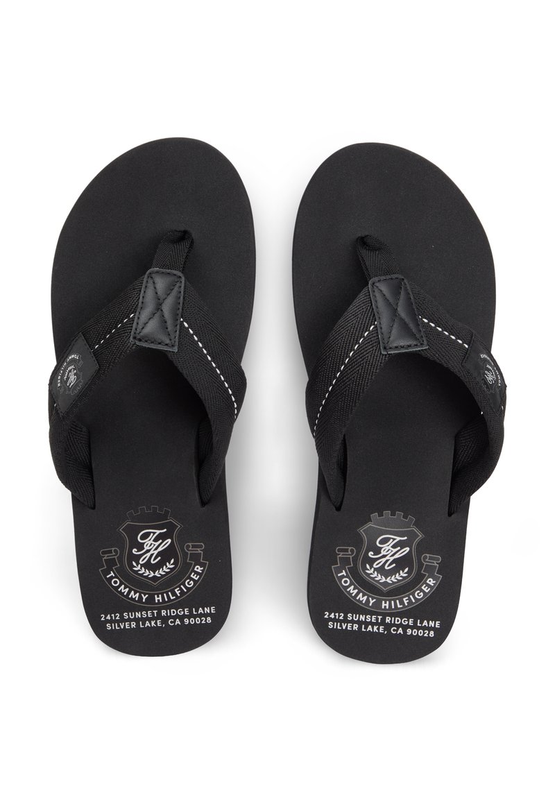 Chanclas negras con suela de goma texturizada y tiras de tela. Presentan detalles con logotipo y costuras blancas en las tiras.