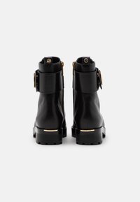 Botas negras de cuero hasta el tobillo con herrajes dorados, cremalleras laterales, un acento de hebilla redonda y una suela de goma texturizada.