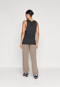 Svart ermeløs tanktopp med teksturert ryggdetalj, parret med lys brune løstsittende bukser og svarte treningssko.