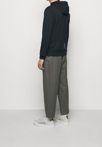 Mörk hoodie med huva och manschettärm, parat med lösa grå byxor och ljusa sneakers. Har reflexdetaljer på baksidan.