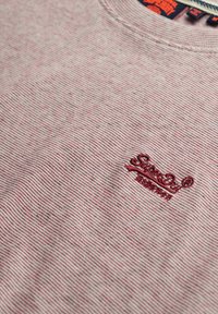 Camiseta de algodón a rayas rojas y blancas con un pequeño logo bordado, cuello redondo y mangas cortas, con un acabado suave y texturizado.
