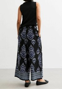 Černé široké kalhoty s modro-bílým zdobeným vzorem, elastickým pasem a dekorativním lemem. Nošeny s černým bezrukávovým topem a černými balerínami.
