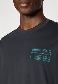 Zwarte korte mouw t-shirt met een ronde hals, voorzien van een turquoise grafische label op de linkerkant van de borst en een zachte katoenen textuur.
