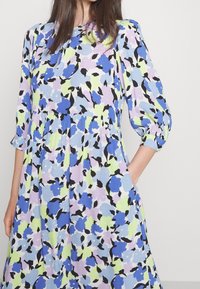 Lichte blauwe bloemenjurk met een kleurrijk patroon van paarse, groene en zwarte accenten. Driekwart mouwen en zijzakken.