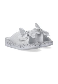 Witte schuifsandalen met een perforatiedesign, voorzien van grote strikken bovenop en een grijs gespikkelde, getextureerde zool. Zacht materiaal voor comfort.