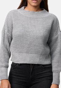 Grå stickad tröja med strukturerat mönster, rund halsringning och ribbade muddar och fåll. Matchas med mörka jeans.