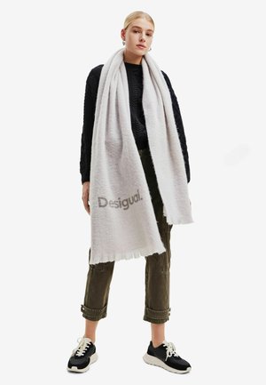 Sciarpa grigia chiara realizzata in un morbido tessuto testurizzato con bordi frangiati. Presenta il logo del marchio "Desigual" in evidenza.