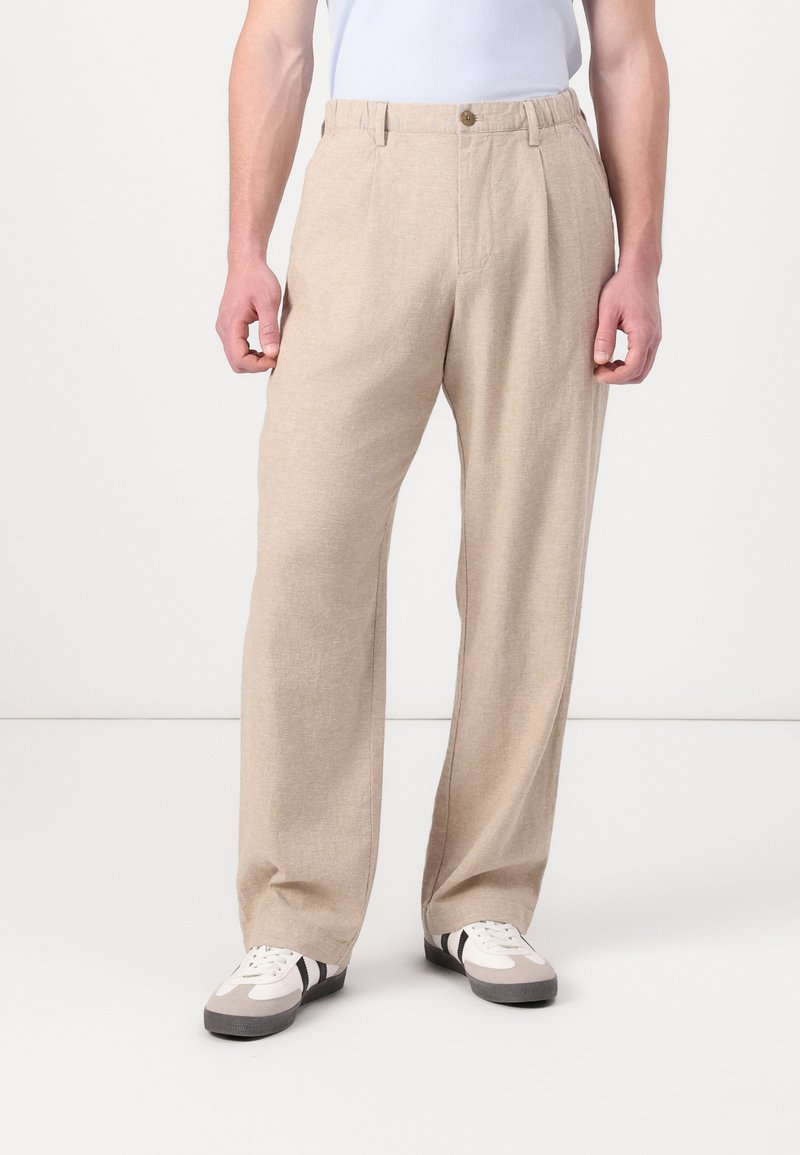 Beige, loose-fitting trousers made of a textured fabric, featuring a button closure, side pockets, and a straight leg design.
