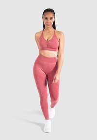 Top corto atlético rojo con detalle fruncido y leggings de tiro alto a juego, ambos en una tela suave y elástica. Lleva puestos zapatillas blancas.