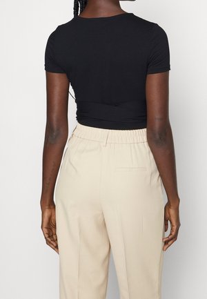 Schwarzes Kurzarmoberteil mit verdrehtem Rückendetail, kombiniert mit beigen Hosen mit elastischem Bund und Gesäßtaschen. Glatte Stoffstruktur.