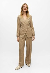 Beige Leinenblazer mit tiefem V-Ausschnitt und zwei Knöpfen, kombiniert mit lockeren, passenden Hosen. Glatte Textur und taillierte Passform.