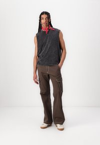 Sleeveless, black acid-wash top paired with brown cargo pants featuring side pockets and contrast stitching. Model wears a red bandana.