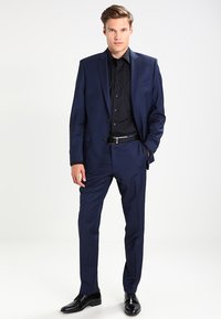 Navy blue suit with tailored jacket and matching trousers, paired with a black shirt. Features a smooth texture and classic design.
