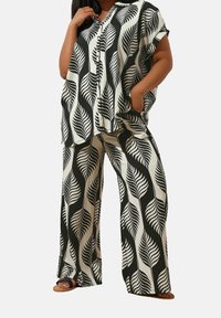 Outfit a fantasia di foglie in bianco e nero con una maglietta morbida dotata di un'apertura con bottoni e pantaloni a gamba larga. Tessuto texturizzato, vestibilità rilassata.