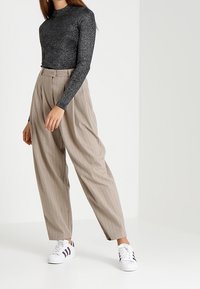 Un haut à manches longues noir pailleté associé à un pantalon beige à rayures verticales taille haute et des baskets blanches avec des rayures foncées.