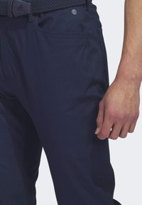 Marineblauwe broek van lichtgewicht stof, met voorzakken en een geweven riem. Subtiele logodetail nabij de tailleband.