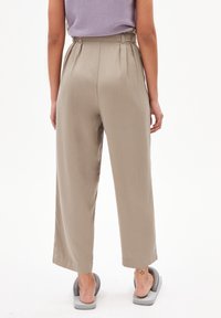 Béžové kalhoty s vysokým pasem a širokými nohavicemi, hladké na dotek a s plisovaným předním detailem, doplněné šedými nazouvacími botami.